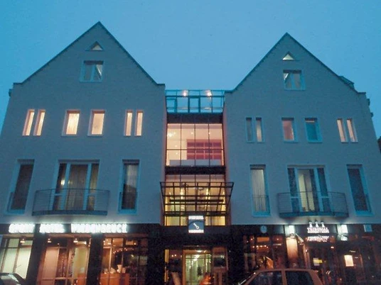 Außenansicht Sporthotel Wiedenbrück Moderne, beleuchtete Hotel-Fassade bei Dämmerung, mit großen Fenstern und Glasüberdachung.