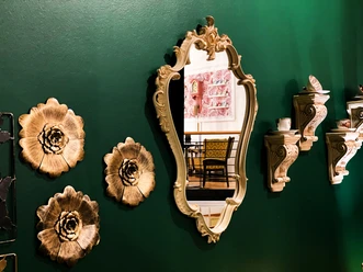 Goldener Spiegel, Blumenreliefs und Kaffeetassen an einer grünen Wand im Café & Bistro Wunderland.