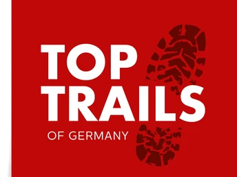 Logo der Top Trails of Germany Logo der "Top Trails of Germany" mit weißem Schriftzug und rotem Hintergrund, ergänzt durch ein Stiefelprofil.