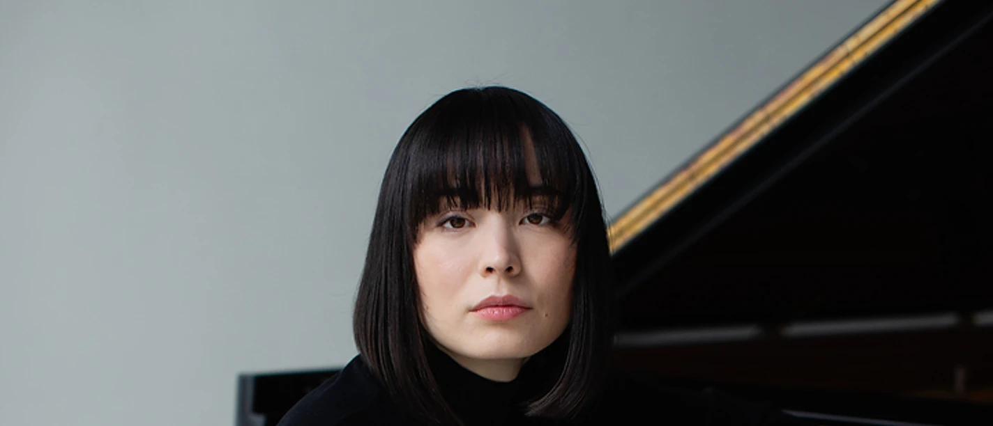Pianist Alice Sara Ott, dressed in black, is sitting on a piano bench at the grand piano.