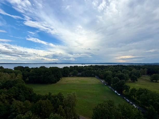 Blick über Wiesen und Wälder auf das Steinhuder Meer unter weitem Wolkenhimmel.