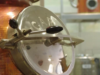 Kupferner Brennkessel mit glänzendem Deckel und präzise gearbeiteter Mechanik in einer Brennerei.