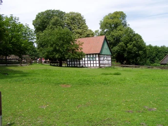 Ravensberger Landschaft Fachwerkhaus umgeben von üppiger Wiese und hohen Bäumen, im Hintergrund weitere ländliche Gebäude.