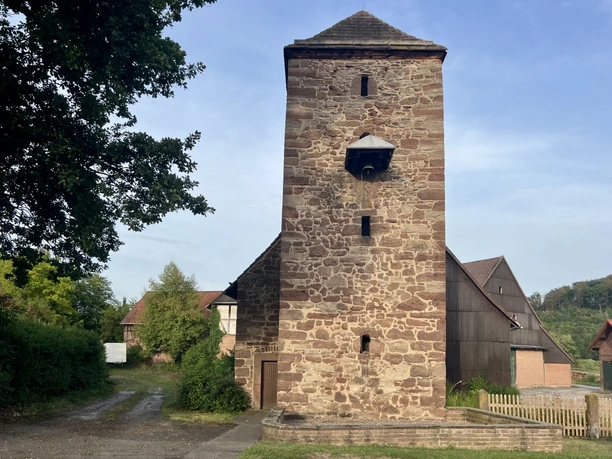 Rötlicher Natursteinturm der Marienkapelle Volksen umgeben von grünen Bäumen.