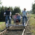 Draisine Familie mit zwei Kindern fährt auf einer Draisine durch eine grüne, von Bäumen gesäumte Landschaft.