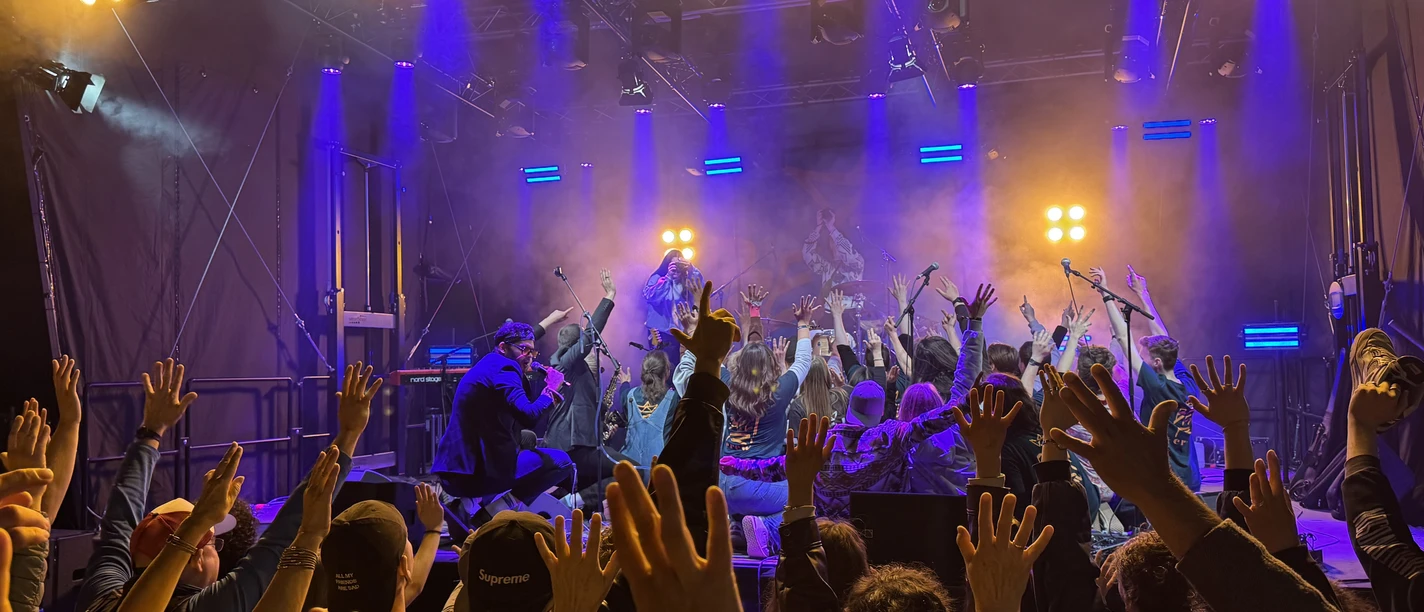 Publikum mit erhobenen Händen vor Festivalbühne in violett-goldenem Licht