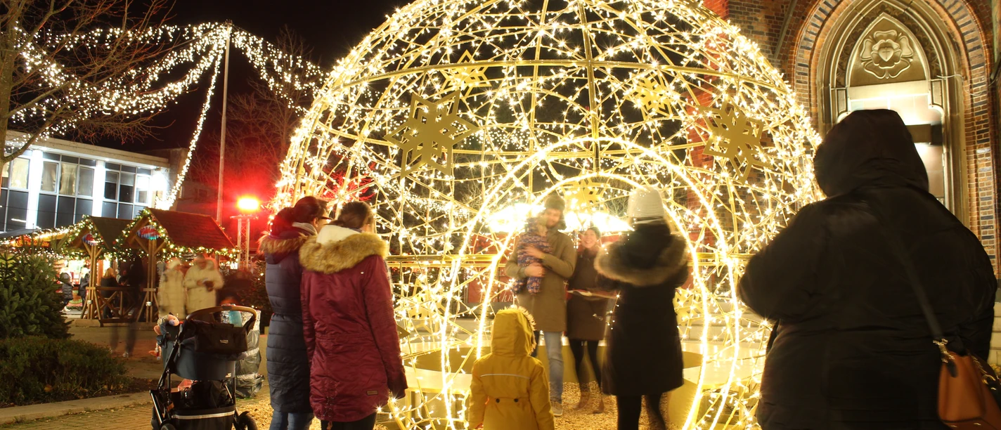 Menschen fotografieren sich in einer großen Lichtkugel auf dem Weihnachtsmarkt.