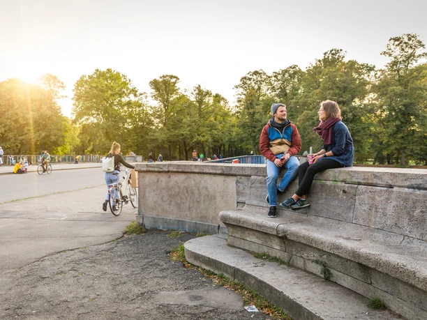 Zwei Personen sitzen bei Sonnenuntergang an der Sachsenbrücke im Clara-Zetkin-Park und unterhalten sich