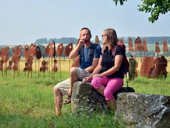 Encore Zwei Personen sitzen auf Steinen und unterhalten sich, im Hintergrund stehen rostrote Skulpturen.