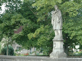 Nepomukbrücke in Steinheim-Vinsebeck Steinerne Statue des Heiligen Nepomuk auf einer Brücke, umgeben von üppigen Bäumen und historischem Gemäuer.