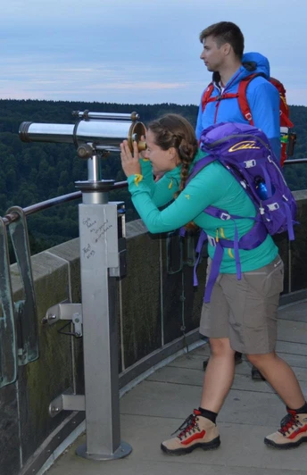 Auf dem Hermannsdenkmal Eine Frau blickt durch ein Fernrohr auf einer Aussichtsplattform, umgeben von Waldlandschaft.