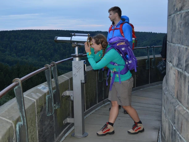 Auf dem Hermannsdenkmal Eine Frau blickt durch ein Fernrohr auf einer Aussichtsplattform, umgeben von Waldlandschaft.