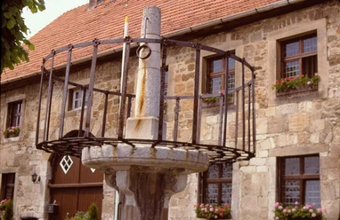 Schandpfahl-Pranger vor Marsberger Rathaus Historischer Pranger aus Stein und Metall vor einem traditionellen Gebäude mit blumengeschmückten Fenstern.