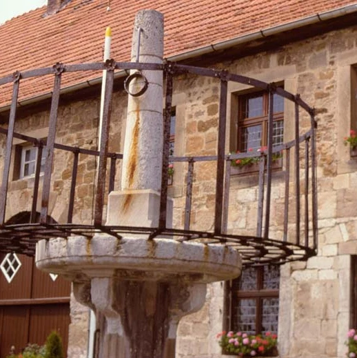 Schandpfahl-Pranger vor Marsberger Rathaus Historischer Pranger aus Stein und Metall vor einem traditionellen Gebäude mit blumengeschmückten Fenstern.
