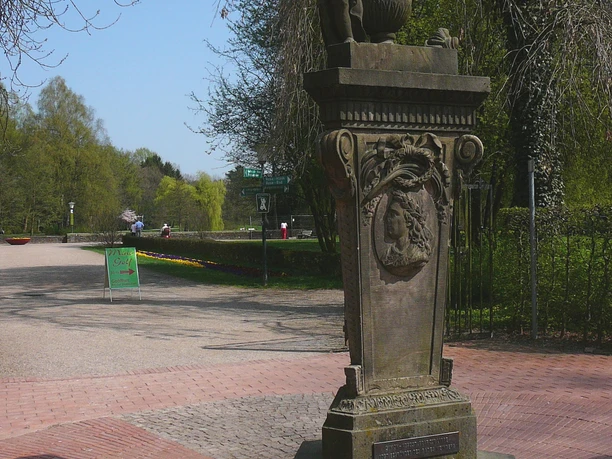 Simon-August-Denkmal auf Sockel am Kurparkweg, umgeben von Bäumen und Pflasterflächen