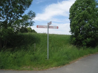 Wegkreuz mit Schildern zu den Orten Oesdorf und Baltringen, umgeben von grünem Gras und Bäumen.