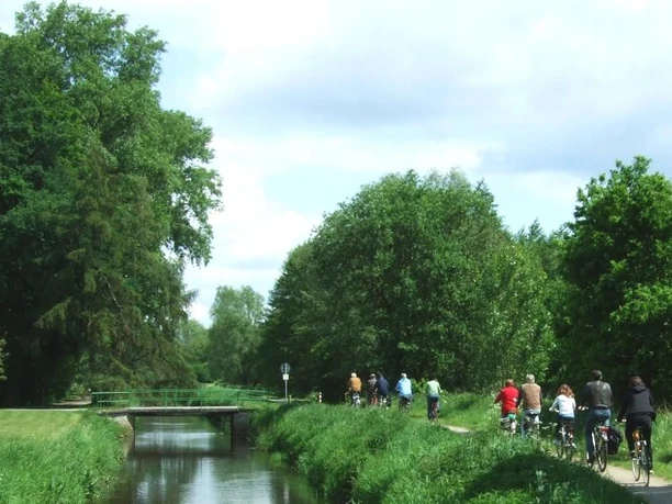 EmsRadweg Gruppe von Radfahrern auf einem naturnahen Weg entlang eines Kanals unter blauem Himmel.