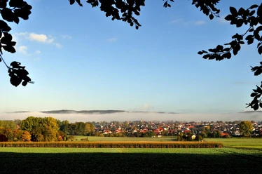 Blick auf Hilter Blick auf die Gemeinde Hilter mit Umrissen im Morgennebel, umgeben von Feldern und Bäumen im Vordergrund.