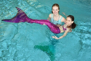 Zwei Mädchen schwimmen im Wellenbad mit glitzernder Meerjungfrauenflosse.