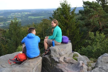 Lippische Velmerstot Zwei Personen sitzen auf Felsen im Lippischen Velmerstot, umgeben von bewaldeter Landschaft.