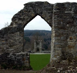 Burgruine Ringelstein Steinerne Ruinen mit einem Torbogen, durch den ein weiteres Burggemäuer und Wald zu sehen sind.