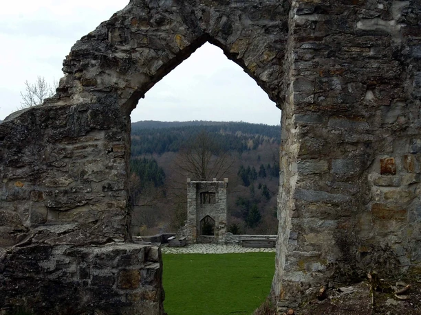 Burgruine Ringelstein Steinerne Ruinen mit einem Torbogen, durch den ein weiteres Burggemäuer und Wald zu sehen sind.