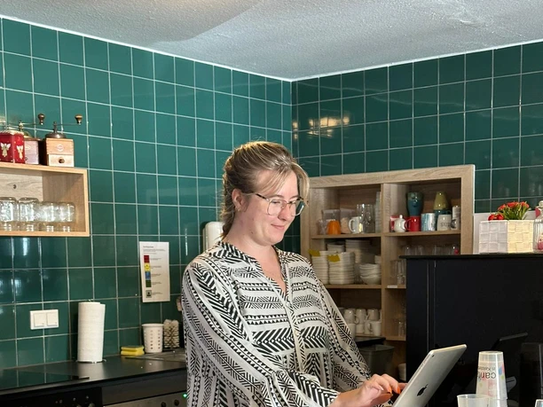 Mitarbeiterin am Kassentresen im Café Lieblingsstück mit grüner Fliesenwand