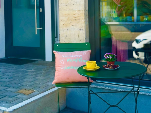 Café Lieblingsstück mit grünem Tisch, gelber Tasse und Sitzbank vor dem Eingang