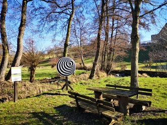 Weg der Sinne Bellersen Ruhiger Rastplatz am „Weg der Sinne Bellersen“: Holztisch mit Bänken und Kunstinstallation in Waldlandschaft.
