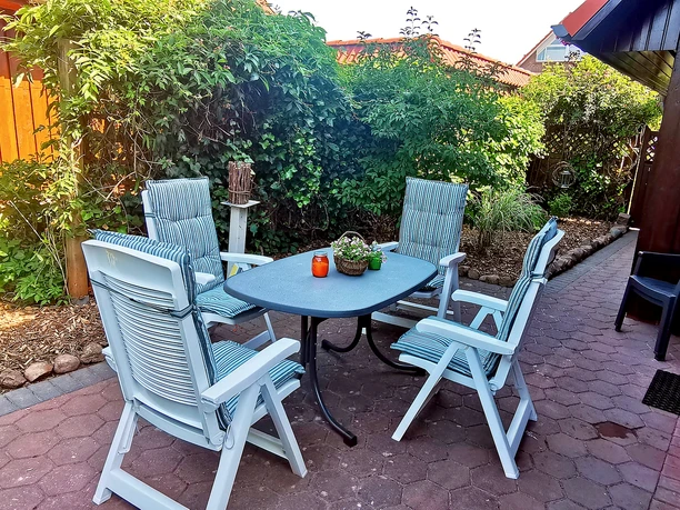 Terrasse Ein schöner Garten mit einem Tisch und vier Stühlen. Die Umgebung ist grün und einladend.