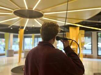 Eine Person steht in der Ausstellung ENERGIE – WAS UNS BEWEGT und hält einen Lautsprecher ans Ohr