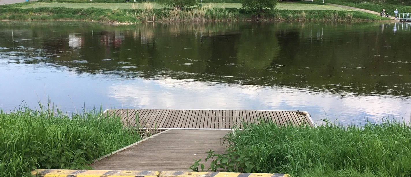 Ein Kanuanleger am Fluss, mit Fähranlegestelle und Gastronomiebetrieb auf der anderen Flussseite.