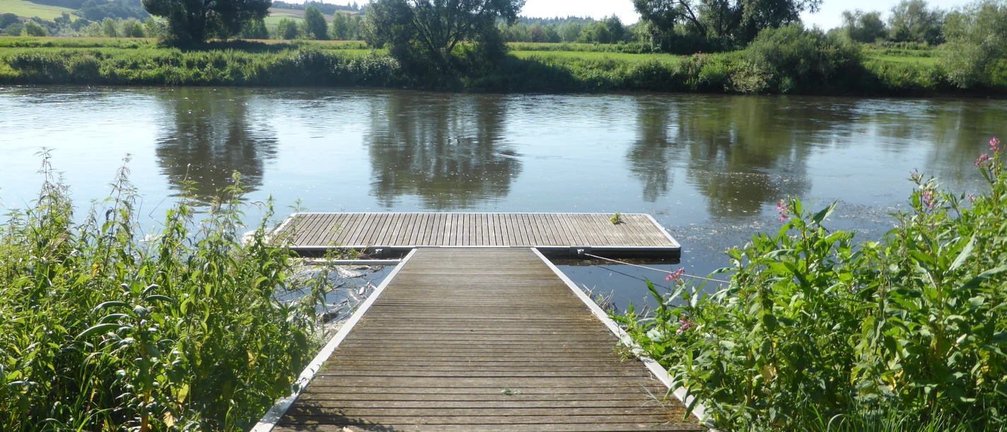 Kanuanleger am Fluss, mit Wiesen und Bäumen an der anderen Flussseite.