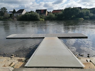 Kanuanleger am Fluss, mit Wohnbebauung an der anderen Flussseite.
