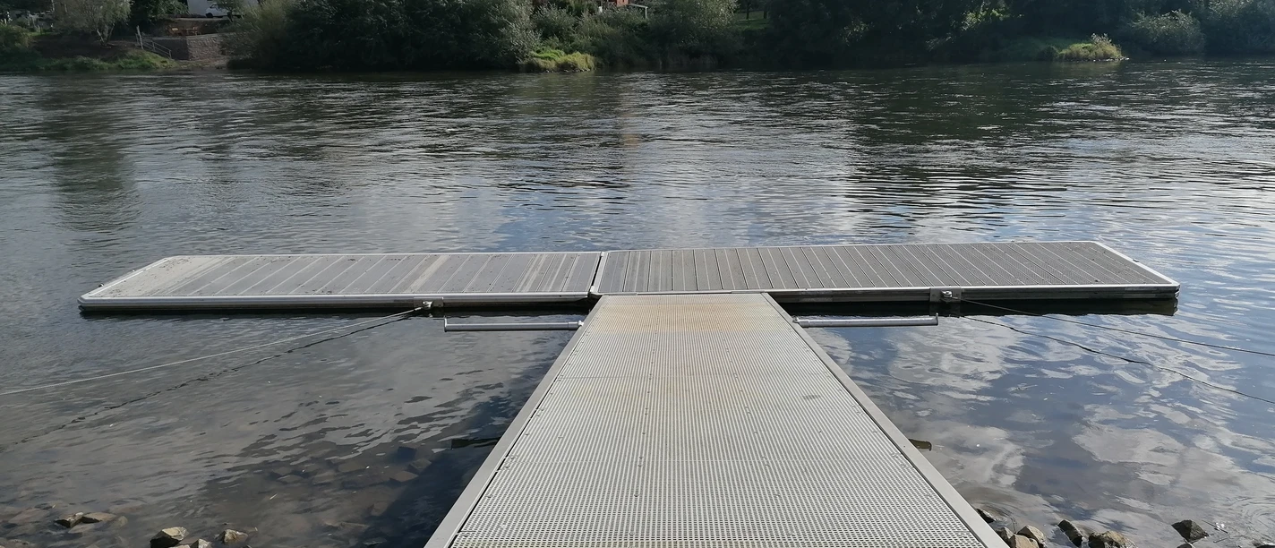 Kanuanleger am Fluss, mit Wohnbebauung an der anderen Flussseite.