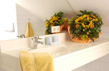 Detailansicht Bad Hotel Römerbad Bad Salzuflen Waschbecken mit einem großen Sonnenblumenarrangement, gelbem Handtuch, zwei Seifen in moderner Badumgebung.