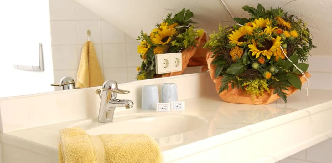 Detailansicht Bad Hotel Römerbad Bad Salzuflen Waschbecken mit einem großen Sonnenblumenarrangement, gelbem Handtuch, zwei Seifen in moderner Badumgebung.