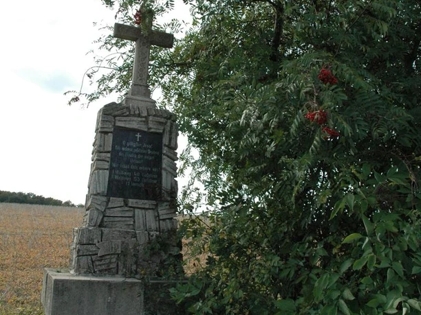 Gefallenen Denkmal Steinernes Kriegerdenkmal mit Kreuz steht neben einem Strauch, umgeben von Feldern und Bäumen.