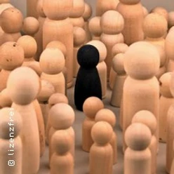 Schwarze Spielfigur steht zwischen vielen hellen Holzfiguren als Symbol für Ausgrenzung