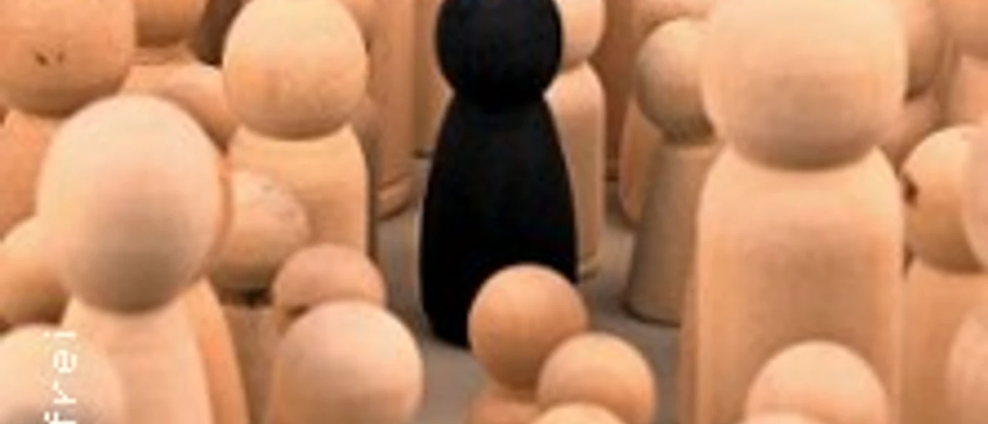 Schwarze Spielfigur steht zwischen vielen hellen Holzfiguren als Symbol für Ausgrenzung