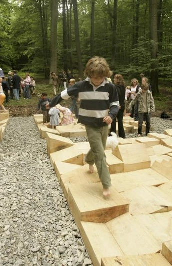 Parkkettinsel Kinder und Erwachsene erkunden barfuß geometrisch gestaltete Holzplattformen in einem Waldgebiet.