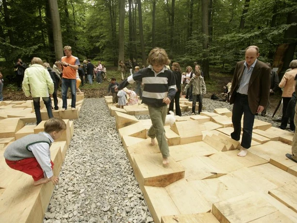 Parkkettinsel Kinder und Erwachsene erkunden barfuß geometrisch gestaltete Holzplattformen in einem Waldgebiet.