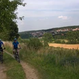 Zwei Radfahrer auf einem Feldweg durch eine weite, grüne Landschaft mit Blick auf ein Dorf.