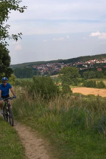 Naturerlebnis im Almetal Zwei Radfahrer auf einem Feldweg durch eine weite, grüne Landschaft mit Blick auf ein Dorf.