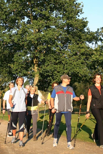 Sechs Menschen beim Nordic Walking auf einem Parkweg, umgeben von grüner Natur und Bäumen.