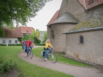 Gruppe von fünf Radfahrern auf einem Weg neben historischen Gebäuden und grüner Wiese.