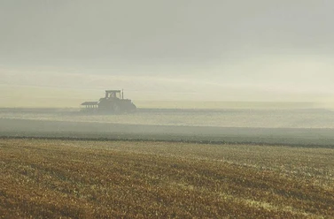 Ein Traktor pflügt ein weites Feld unter bewölktem Himmel, in einer ländlichen und ruhigen Umgebung.
