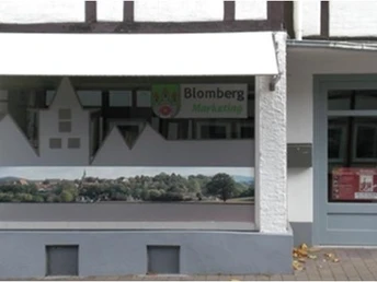 Geschäftsfassade mit Werbefenster und Aufschrift "Blomberg Marketing" in einer Fußgängerzone.