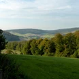Weserhoehen_Blick_ins_Nethetal_oberhalb_Bruchhausen Weitläufige Ansicht über bewaldete Hügel und grüne Wiesen mit sanftem Sonnenlicht im Nethetal.