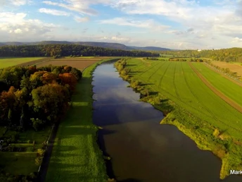 Weserhoehen_Weserpartie_Wehrden Blick von oben auf einen ruhigen Fluss inmitten weitläufiger Felder und Wälder unter blauem Himmel.
